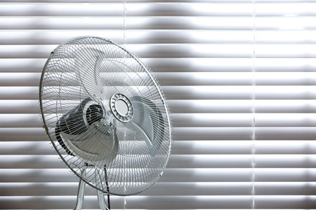Modern electric fan near window indoors. Space for textの写真素材
