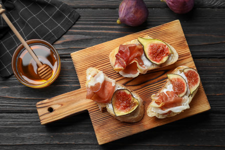 Sandwiches with ripe figs, prosciutto and cream cheese served on black wooden table, flat layの写真素材