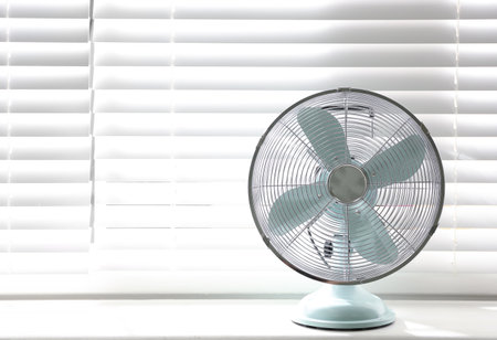 Modern electric fan on window sill indoors. Space for textの写真素材