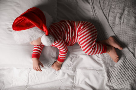 Baby in Santa hat sleeping on bed with white linens, top viewの写真素材
