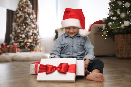 Cute little boy opening gift box in room decorated for Christmasの写真素材