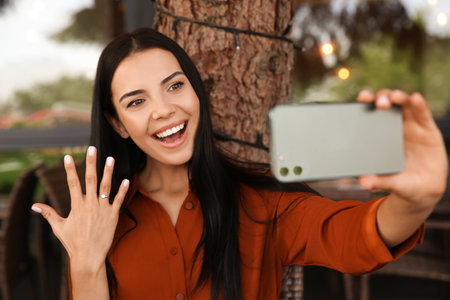 Happy woman with engagement ring taking selfie in outdoor cafeの写真素材