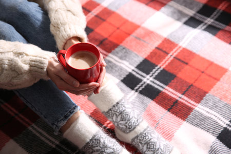 Woman relaxing with cup of hot winter drink on checkered plaid, closeup. Space for textの写真素材