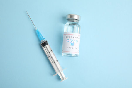 Vial with coronavirus vaccine and syringe on light blue background, flat layの写真素材