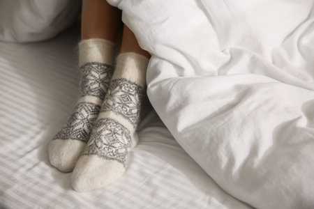 Woman wearing knitted socks under blanket in bed, closeupの写真素材