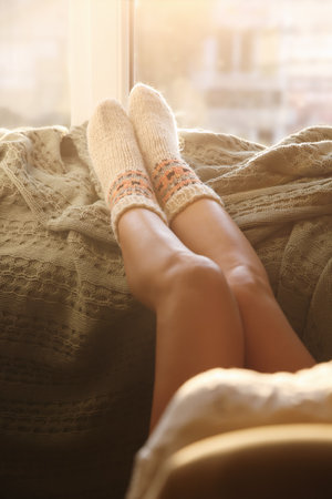 Woman in knitted socks relaxing on plaid near window at home, closeupの写真素材