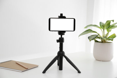 Smartphone with blank screen fixed to tripod on white table indoors. Mockup for designの写真素材