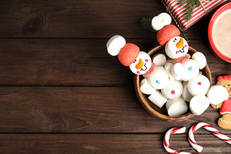 Flat lay composition with funny snowmen made of marshmallows in bowl on wooden table, space for textの写真素材
