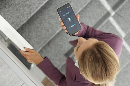 Young woman using voice search on smartphone indoors, above view
