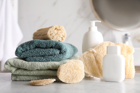 Natural loofah sponges, towels and cosmetic products on table in bathroom