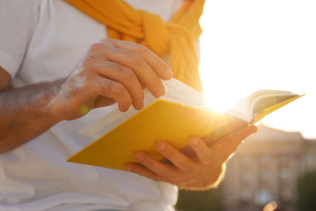 Young man reading book outdoors on sunny day, closeupの写真素材
