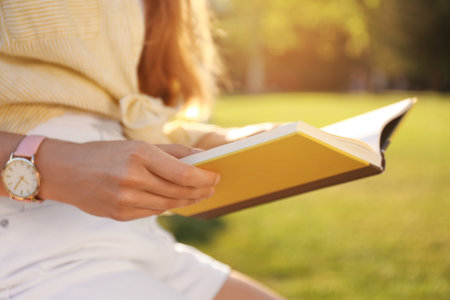 Young woman reading book outdoors on sunny day, closeupの写真素材