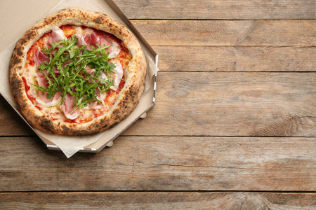Tasty pizza with meat and arugula in cardboard box on wooden table, top view. Space for textの写真素材