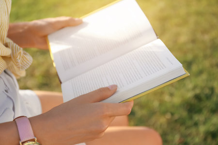 Young woman reading book outdoors on sunny day, closeupの写真素材