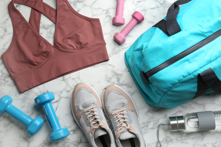 Flat lay composition with gym bag and sportswear on white marble table