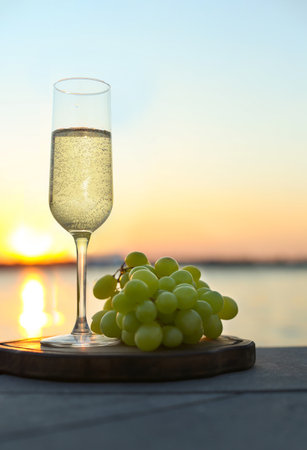 Glass of champagne and fresh grapes served near river at sunsetの写真素材