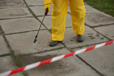 Person in hazmat suit disinfecting street pavement with sprayer, closeup.の写真素材