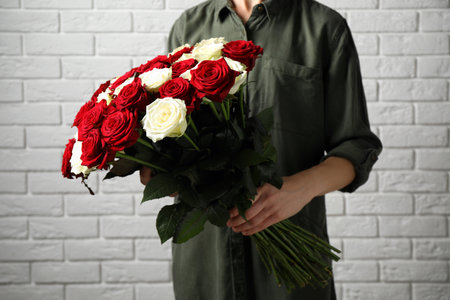Woman holding luxury bouquet of fresh roses near white brick wall, closeupの写真素材