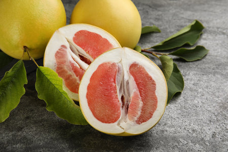 Fresh cut and whole pomelo fruits with leaves on gray table