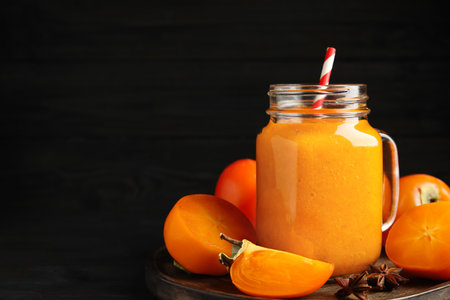 Tasty persimmon smoothie with straw and fresh fruits on table against black background. Space for textの写真素材