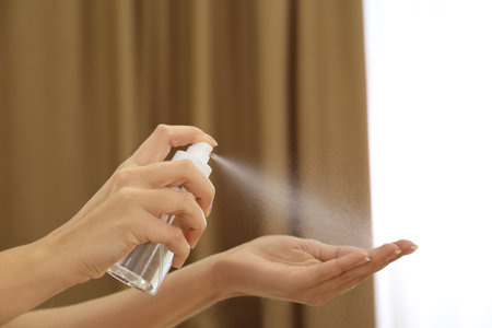 Woman spraying antiseptic onto hand indoors, closeupの写真素材