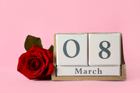 Wooden block calendar with date 8th of March and rose on pink background, space for text....