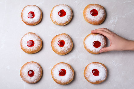 Woman taking Hanukkah donut with jelly and sugar powder at gray table, top viewの写真素材