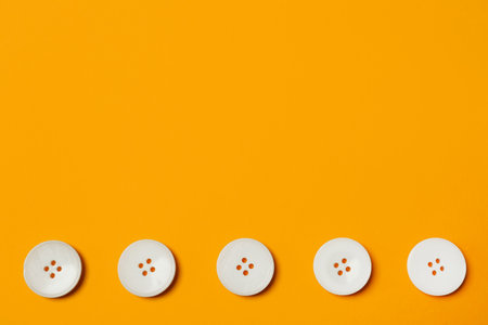 Line of white buttons on orange background, flat lay. Space for textの写真素材