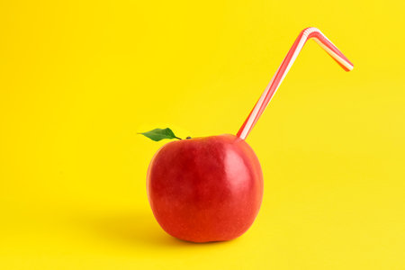 Fresh apple with straw on yellow background. natural juice conceptの写真素材