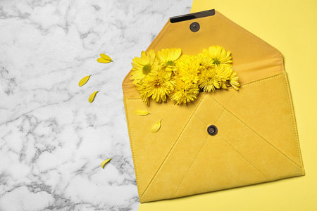 Beautiful women's clutch and chrysanthemum flowers on white marble background, flat lay. Space for textの写真素材