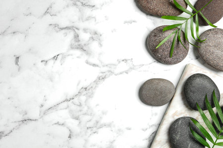 Spa stones and green leaves on white marble table, flat lay. Space for textの写真素材