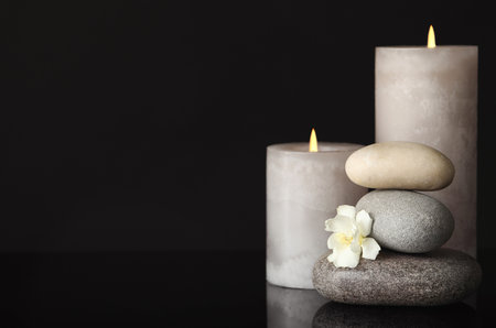 Stack of spa stones, burning candles and fresh flower on black background. Space for textの写真素材