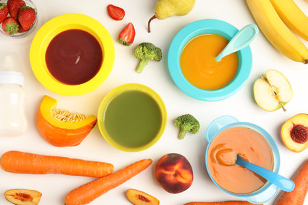 Baby food in bowls and fresh ingredients on white table, flat layの写真素材