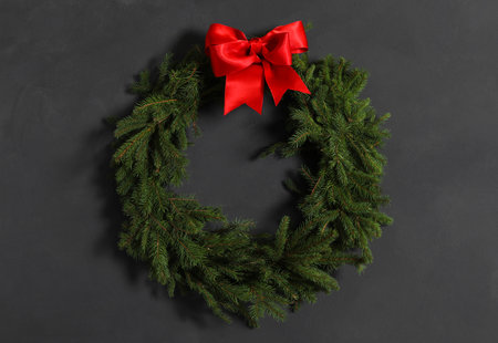 Christmas wreath made of fir branches with red bow on black wallの写真素材