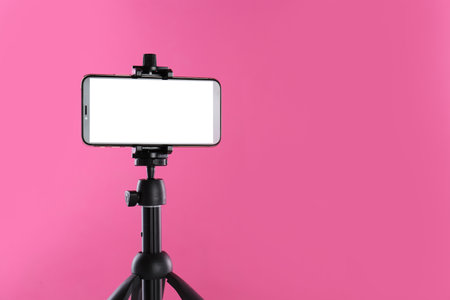 Smartphone with blank screen fixed to tripod on pink background. Space for textの写真素材
