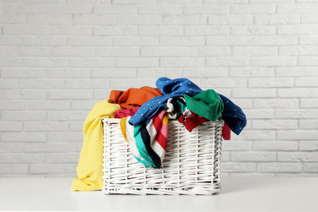 Wicker basket with laundry on table near white brick wall