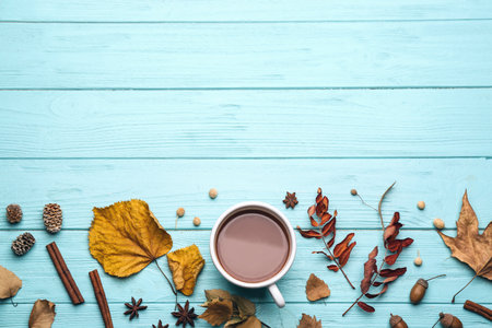 Flat lay composition with cup of hot drink and autumn leaves on light blue wooden table, space for...