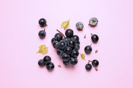 Bunch of ripe dark blue grapes with leaves on pink background, flat layの写真素材