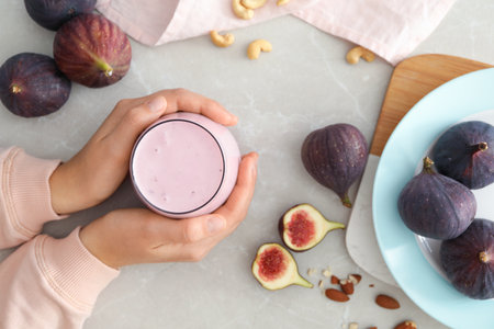 Woman with delicious fig smoothie at light table, top viewの写真素材