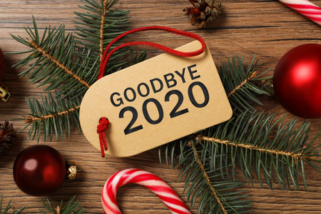Tag with text Goodbye 2020 and festive decor on wooden background, flat layの写真素材