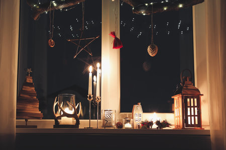 Burning candles and Christmas decor on window sill at nightの写真素材