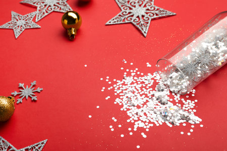 Composition with shiny confetti spilled out of champagne glass near Christmas decorations on red background, closeupの写真素材