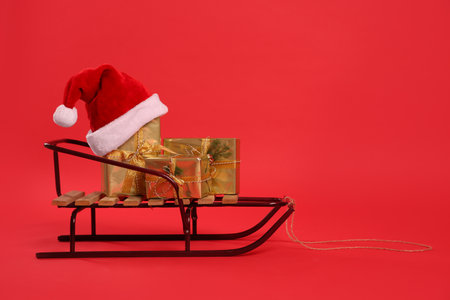Sleigh with gift boxes and Santa hat on red background. Space for textの写真素材
