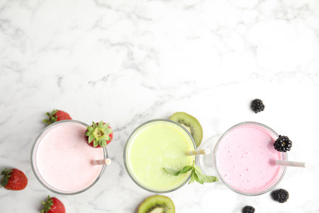 Tasty fresh milk shakes with fresh berries on white marble table, flat lay. Space for textの写真素材