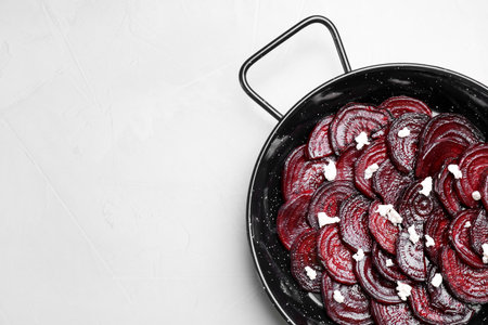 Roasted beetroot slices with feta cheese in wok pan on light gray table, top view. Space for textの写真素材