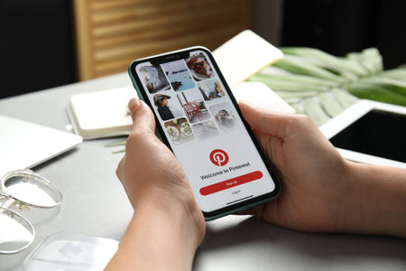 MYKOLAIV, UKRAINE - JULY 9, 2020: Woman holding Iphone 11 with Pinterest app on screen at table, closeupのeditorial素材