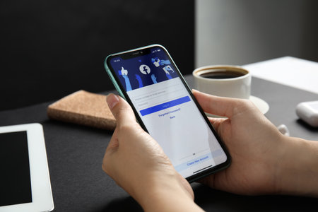MYKOLAIV, UKRAINE - JULY 9, 2020: Woman holding Iphone 11 with Facebook app on screen at black table, closeupのeditorial素材