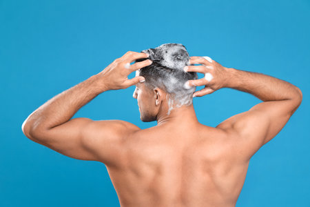 Handsome man washing hair on light blue background, back viewの写真素材