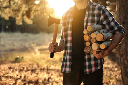 Man holding pile of cut firewood and ax in forest, closeupの写真素材