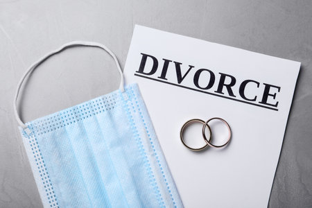 Flat lay composition with protective mask and wedding rings on gray table. Divorce during coronavirus quarantineの写真素材